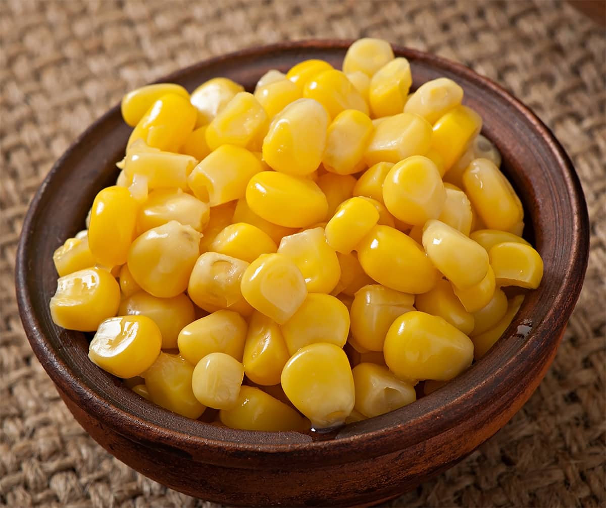 A bowl of freshly boiled corn kernels with a sprig of parsley