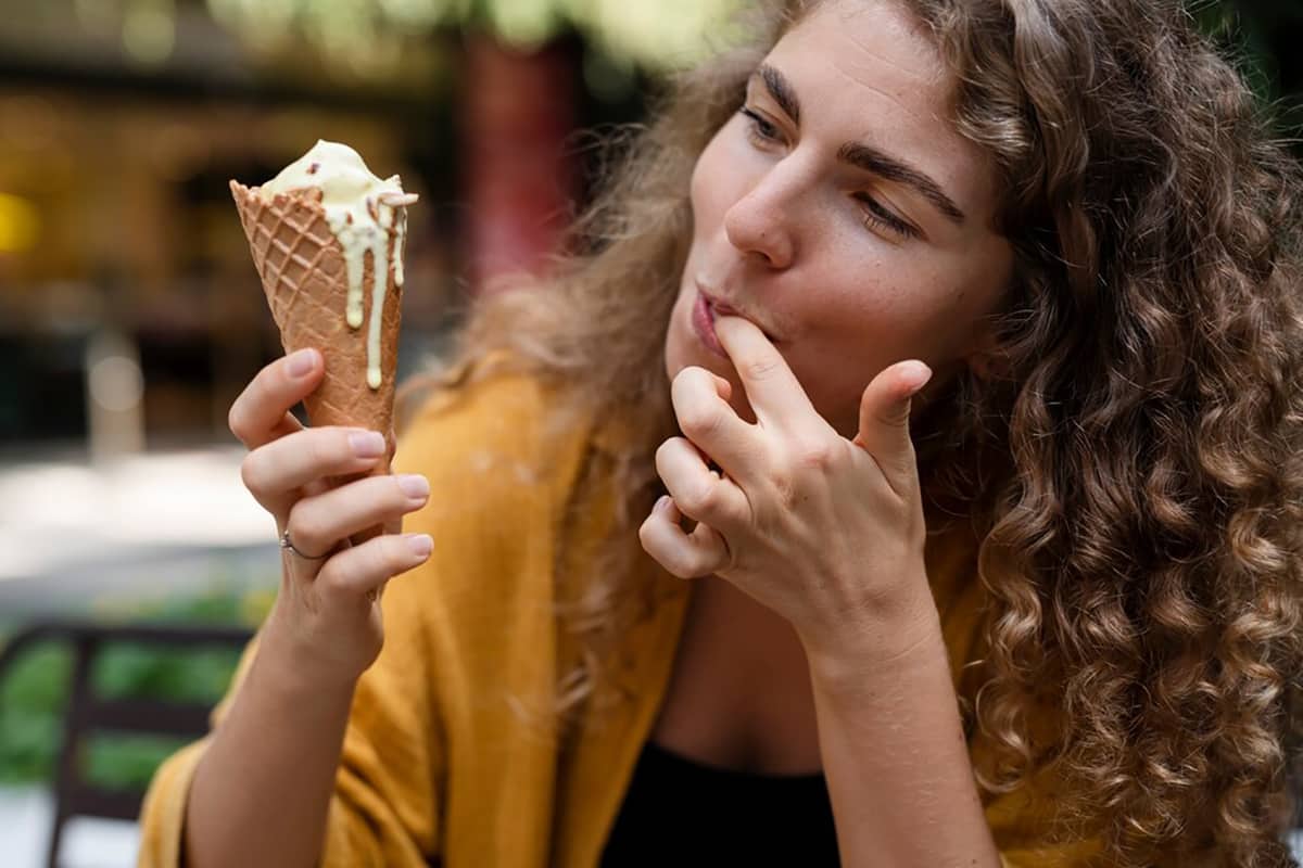 Young woman enjoying an ice cream cone while licking her finger, representing a craving moment